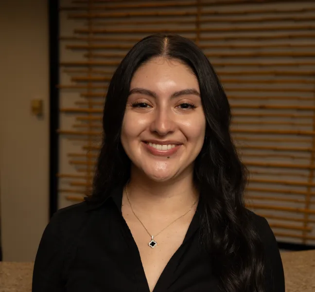 Smiling woman with long dark hair wearing a black shirt and a pendant necklace.