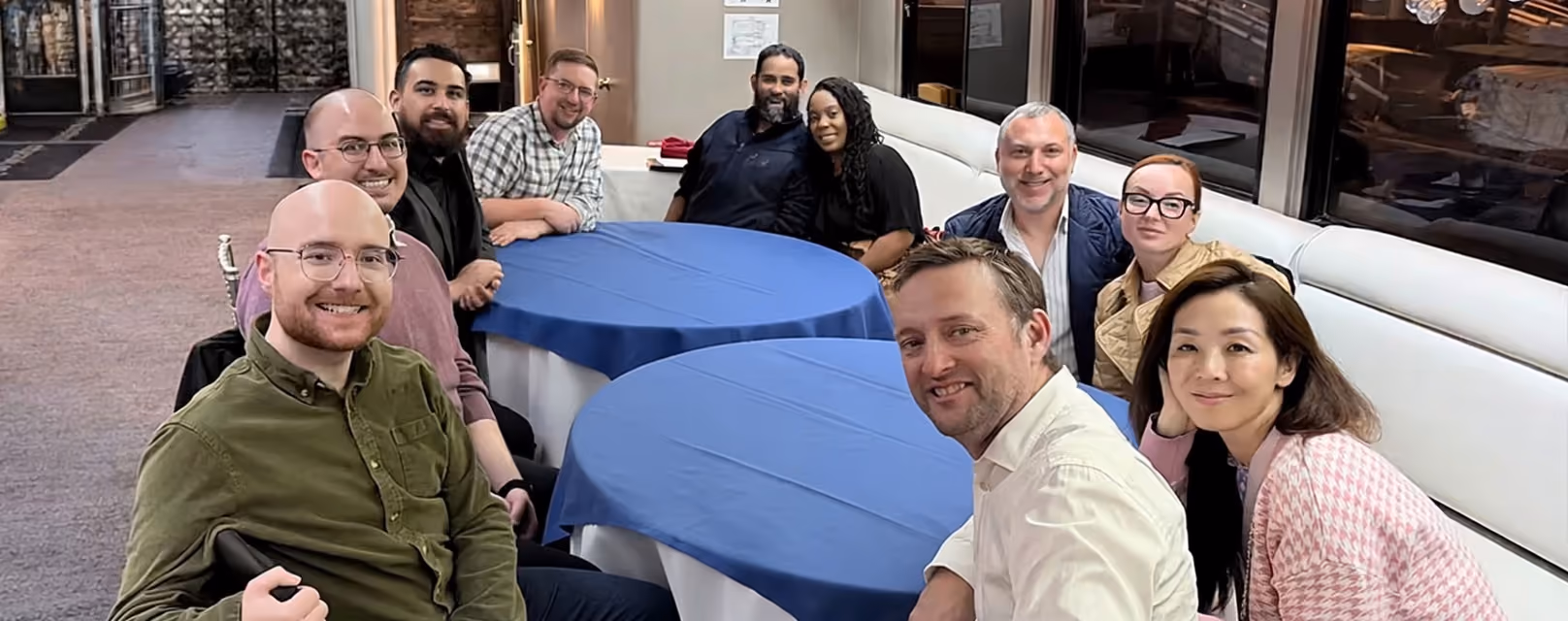 Group of eleven people sitting around a table with blue tablecloth, smiling at the camera.