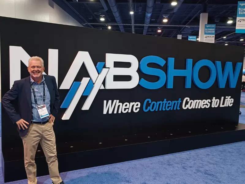 Mark Lay, VP of Sales and Business Development at Arcadian, poses smiling in front of a large NAB Show 2025 sign in Las Vegas. The backdrop reads 'Where Content Comes to Life' with bold white and blue lettering at a media exhibition venue.