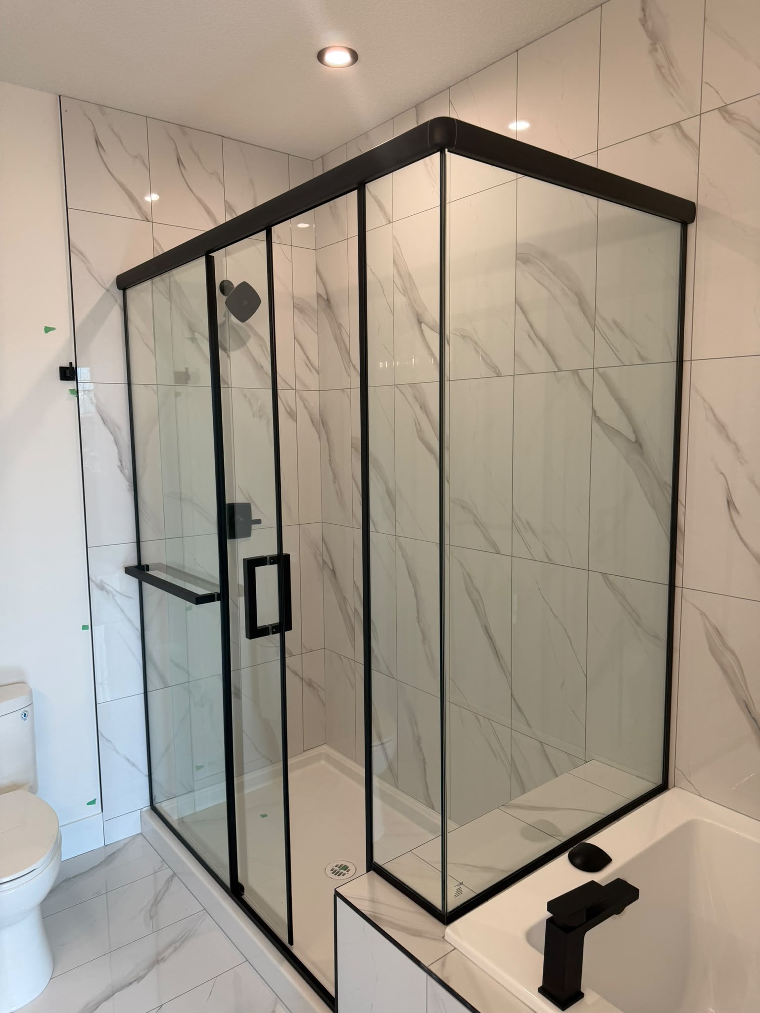 a custom shower door in black hardware that is installed by the expert team of oz shower doors in Edmonton