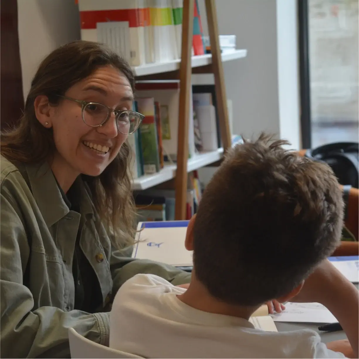 A woman and a boy are sitting at a table with books and papers.