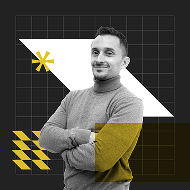 A man in a gray turtleneck sweater stands confidently with arms crossed in front of a dark background featuring geometric shapes in yellow and white.