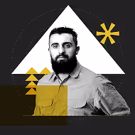 A man with a beard wearing a gray shirt, standing against a black background with geometric shapes in white and yellow.