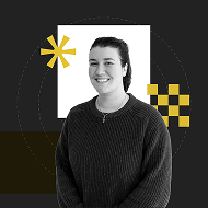 A smiling woman wearing a dark sweater stands against a black background with geometric shapes in white and yellow. She has her hair pulled back and is facing the camera.