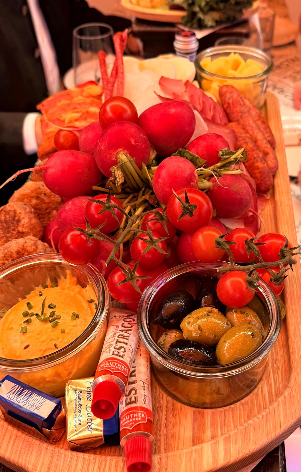 A Brotzeit board with radishes, tomatoes, olives, cheese and cold cuts