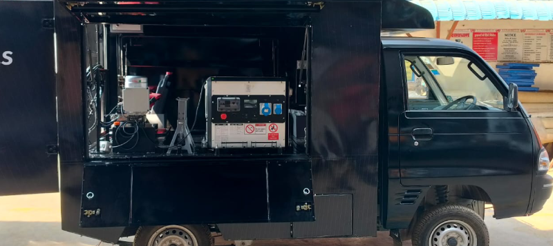 Black utility vehicle with an open side compartment showing electronic and mechanical equipment inside.
