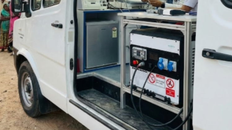 Open side door of a white van showing electronic equipment and a small refrigerator inside.