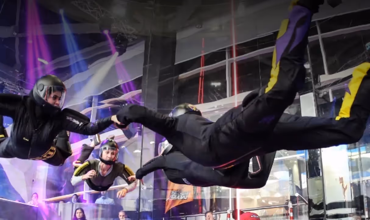 Four people in skydiving suits and helmets indoor flying and holding hands in a vertical wind tunnel.