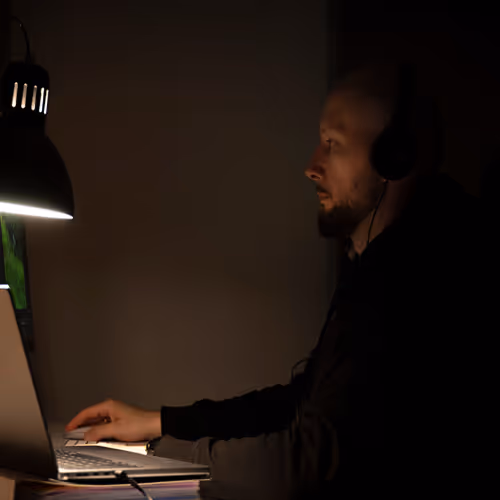 Mateusz Mrozek, projektant stron internetowych, pracujący w nocy przed dużym monitorem. Zdjęcie symbolizuje zaangażowanie w tworzenie stron WWW.