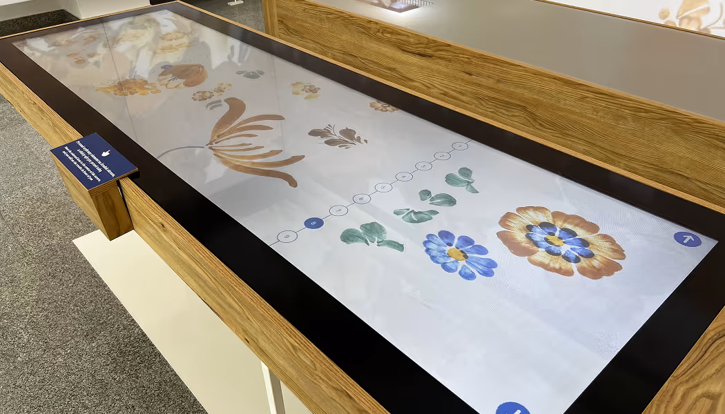 Zbliżenie na ekran dotykowy z aplikacją do tworzenia fajansowych wzorów w Skarbcu Fajansu. Widoczny interfejs UI designu aplikacji muzealnej.