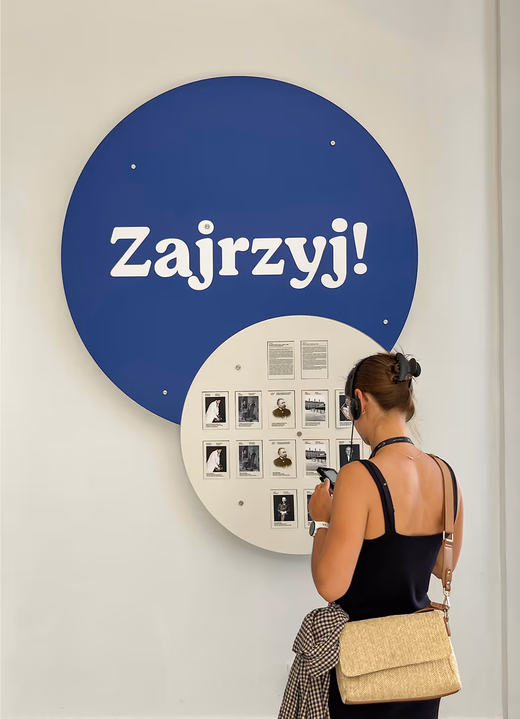 Zwiedzająca czytająca obrotową tabliczkę z informacjami o osobach związanych z fajansem. Element wystawy stałej Skarbca Fajansu, prezentujący życiorysy twórców.