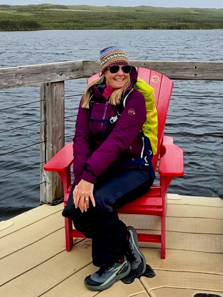 lady strikes pose on parks Canada red chairs in pei