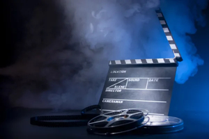 Film clapperboard with empty fields and two vintage film reels against a smoky blue and black background.