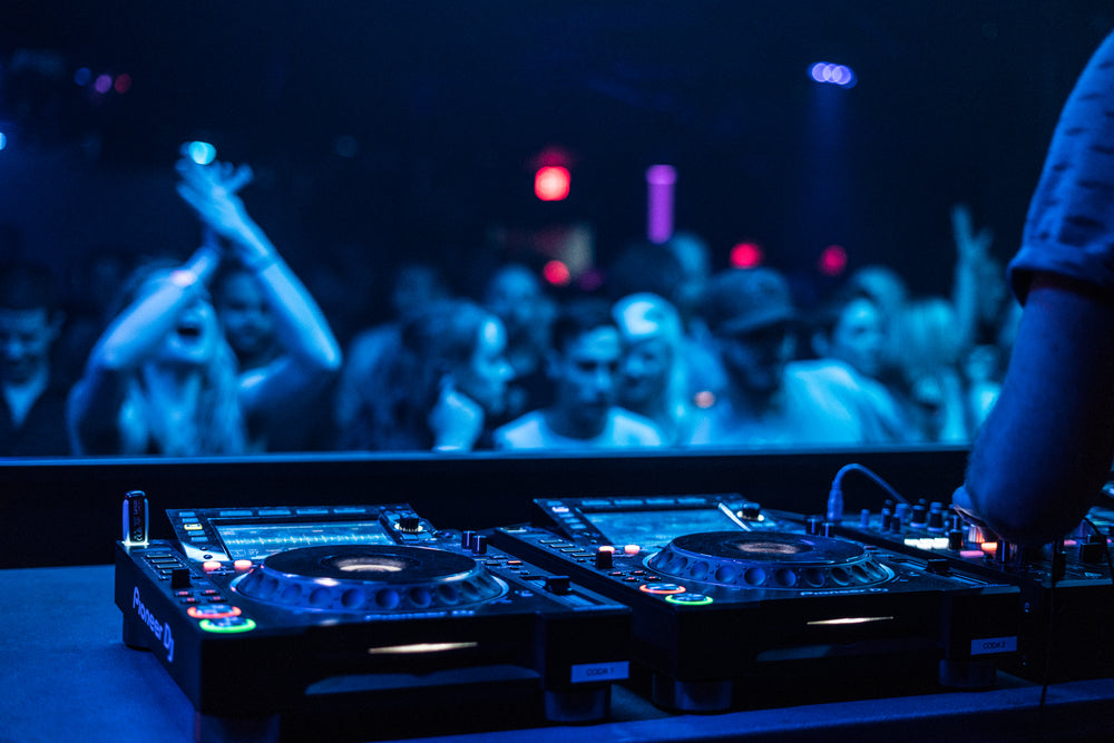 DJ mixing on turntables with a crowd dancing and cheering in the background under blue lighting.