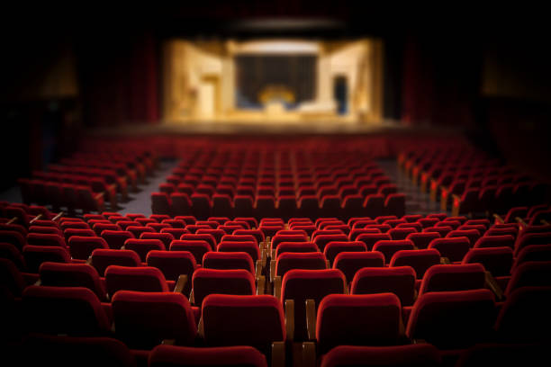 Empty theater auditorium with rows of red seats facing a lit stage in the background.