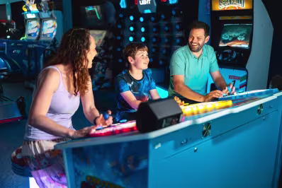 A woman, a young boy, and a man smiling and playing an arcade game together.