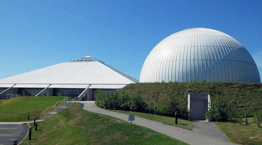 Modern science center with a large white dome and pyramid-shaped building under a clear blue sky.