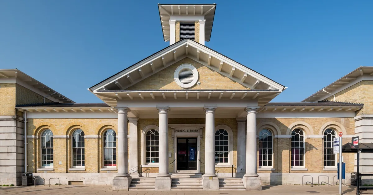 Front facade of a public library building with six white columns, arched windows, and a clear blue sky.