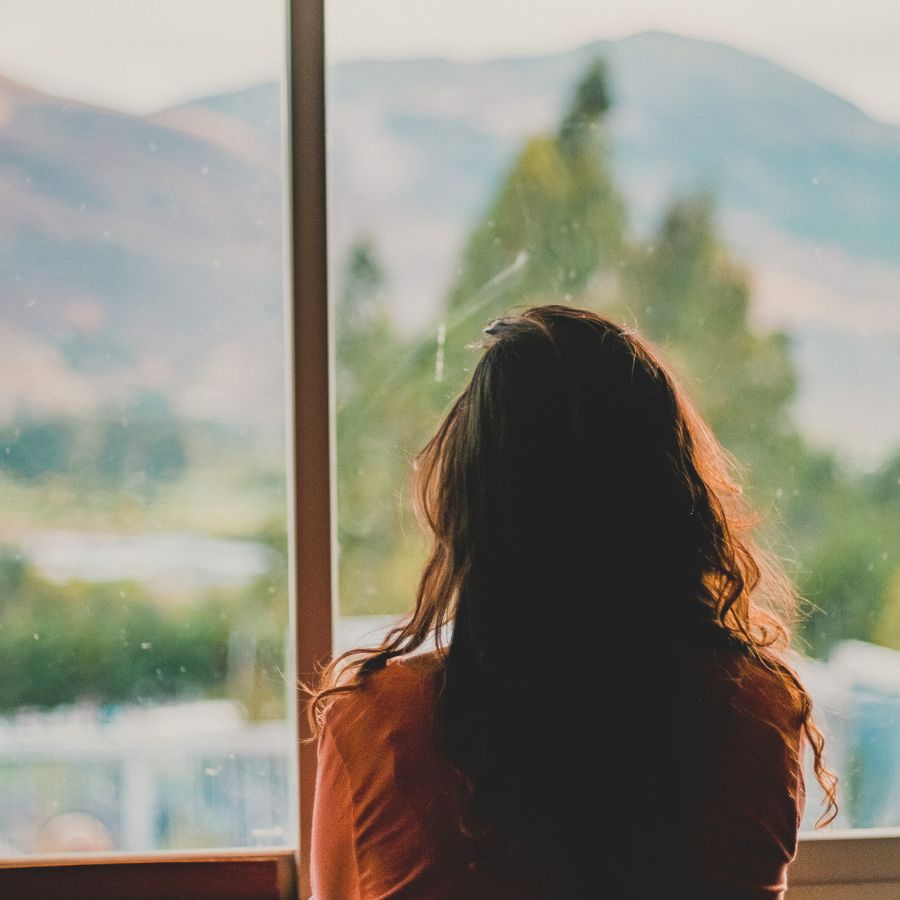 Woman looks out of window into nature, seemingly lost in thought - how to stop overthinking.