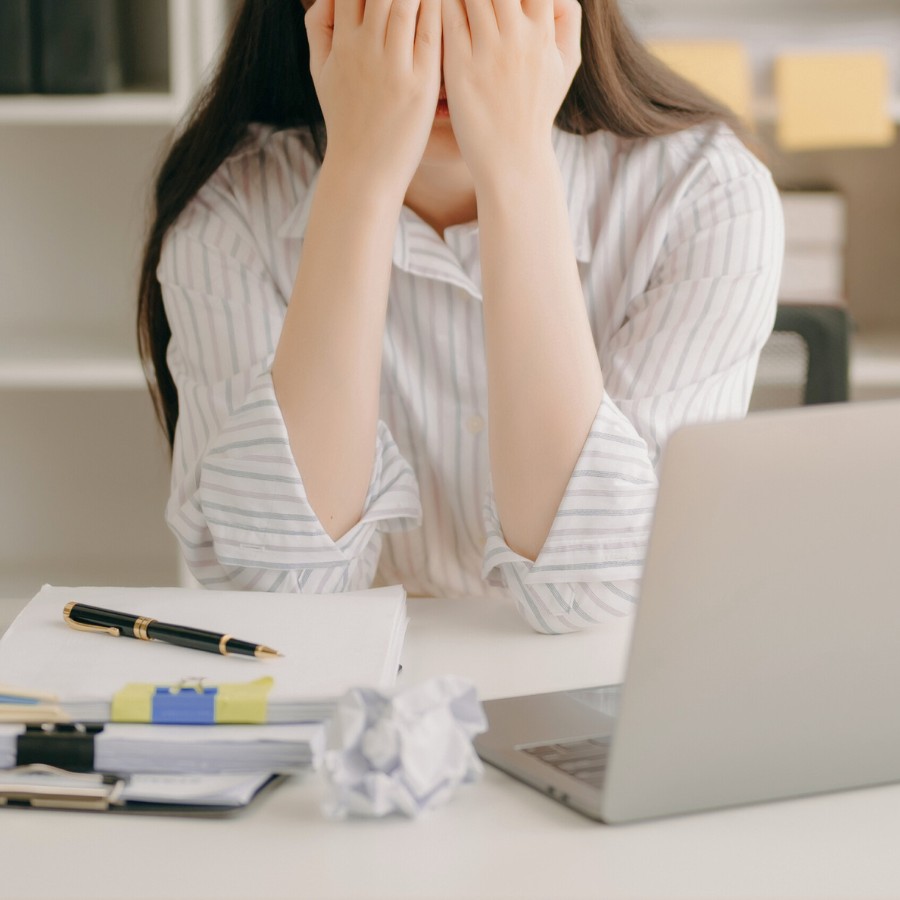 Woman with high-functioning anxiety sitting at desk with open laptop and notes, but not able to work.
