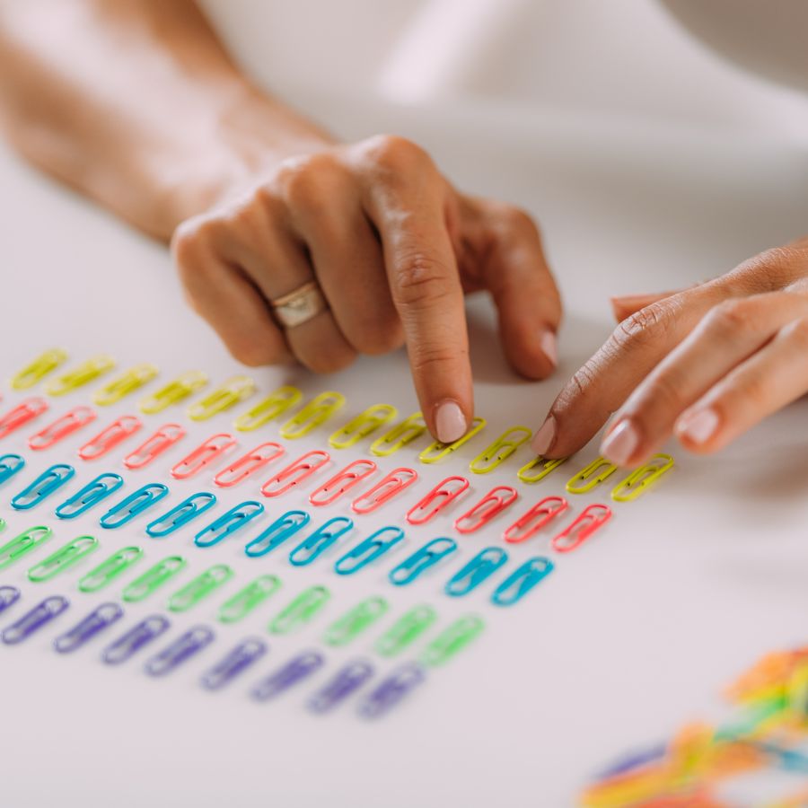 A woman's hands organizing paper clips into rows by color.