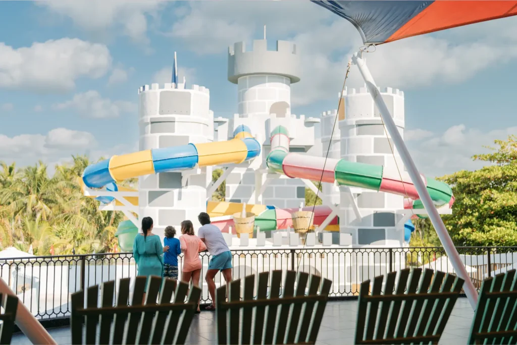 Family looking at a colorful waterslide castle in an amusement park with blue skies and palm trees.