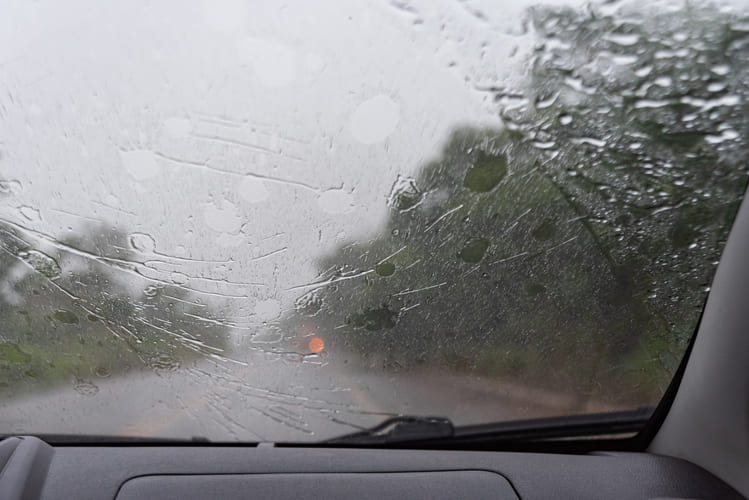 Parabrisas de auto con lluvia intensa para representar manejo durante mal clima y temporada de huracanes Cancun Hiweb
