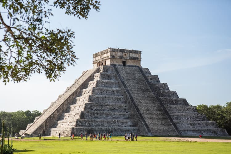 The pyramid of Chichén Itzá rises above the surrounding grounds as visitors gather below, showing one of Yucatán’s most iconic landmarks that travelers can reach more comfortably with a rental car from Avant