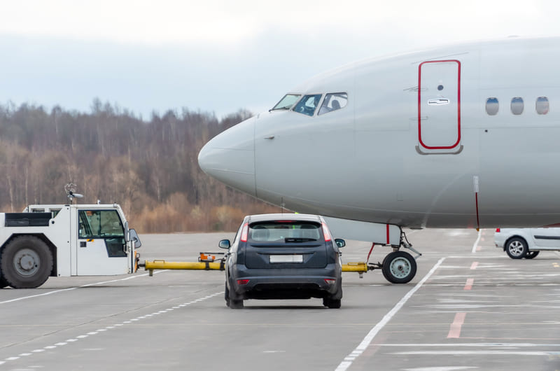 Un auto espera en la pista del aeropuerto cerca de un avión y un vehículo de servicio, mostrando una escena de traslado donde la movilidad confiable facilita llegadas y salidas con Avant
