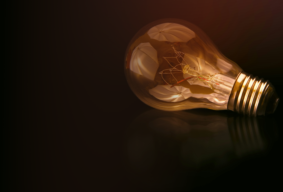 Eine Glühbirne mit sichtbarem Glühdraht und reflektierenden Oberflächen, auf einem dunklen Hintergrund.