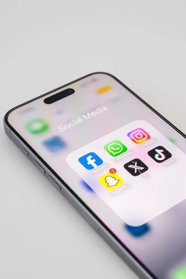 Eine Close-Up Ansicht auf einem Smartphone zeigt den Bildschirm mit einem Ordner namens "Social Media", der die Apps Facebook, WhatsApp, Instagram, Snapchat, X und TikTok enthält.