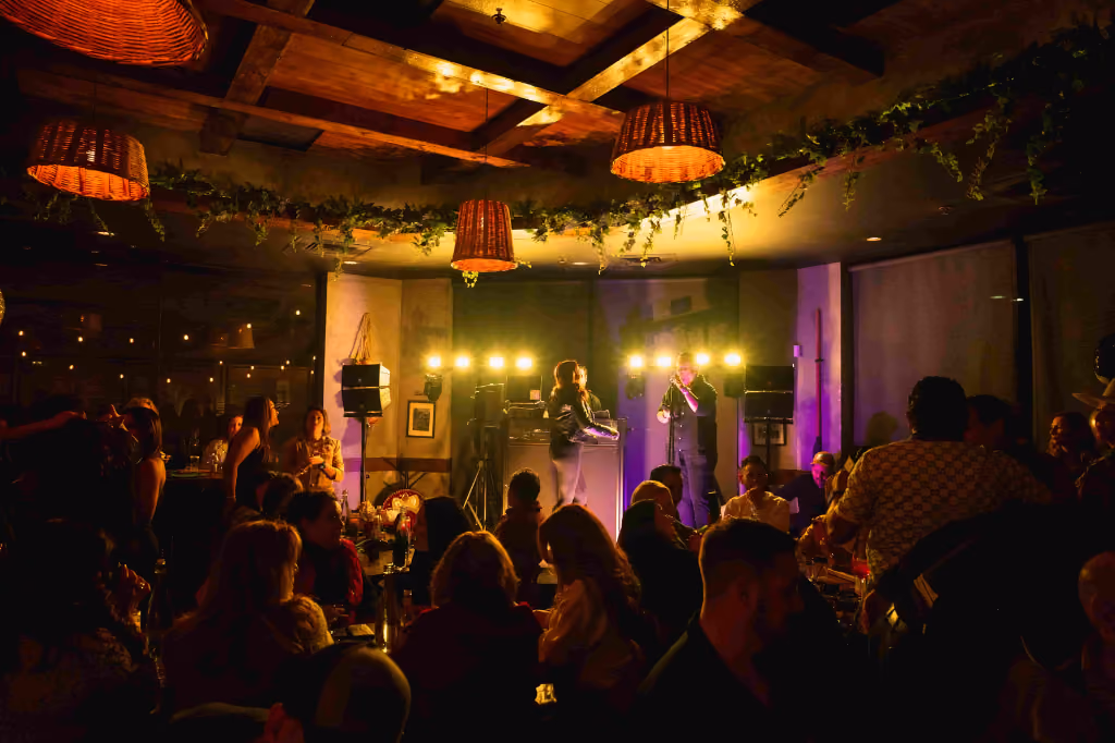 Dimly lit music venue with live band performing and audience seated at tables.