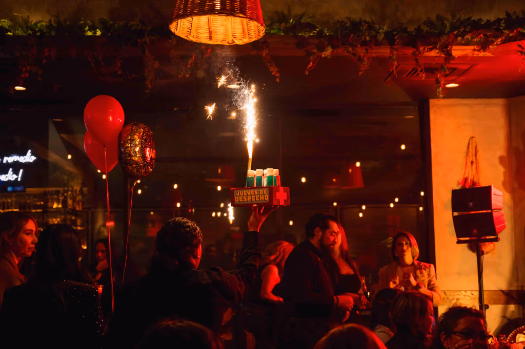 Party scene with people, red balloons, and a tray with sparklers lit in a dimly lit room.