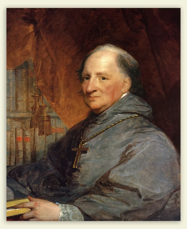Portrait of a smiling clergyman wearing grey robes and a large gold cross necklace holding a book, with bookshelves and a curtain in the background.