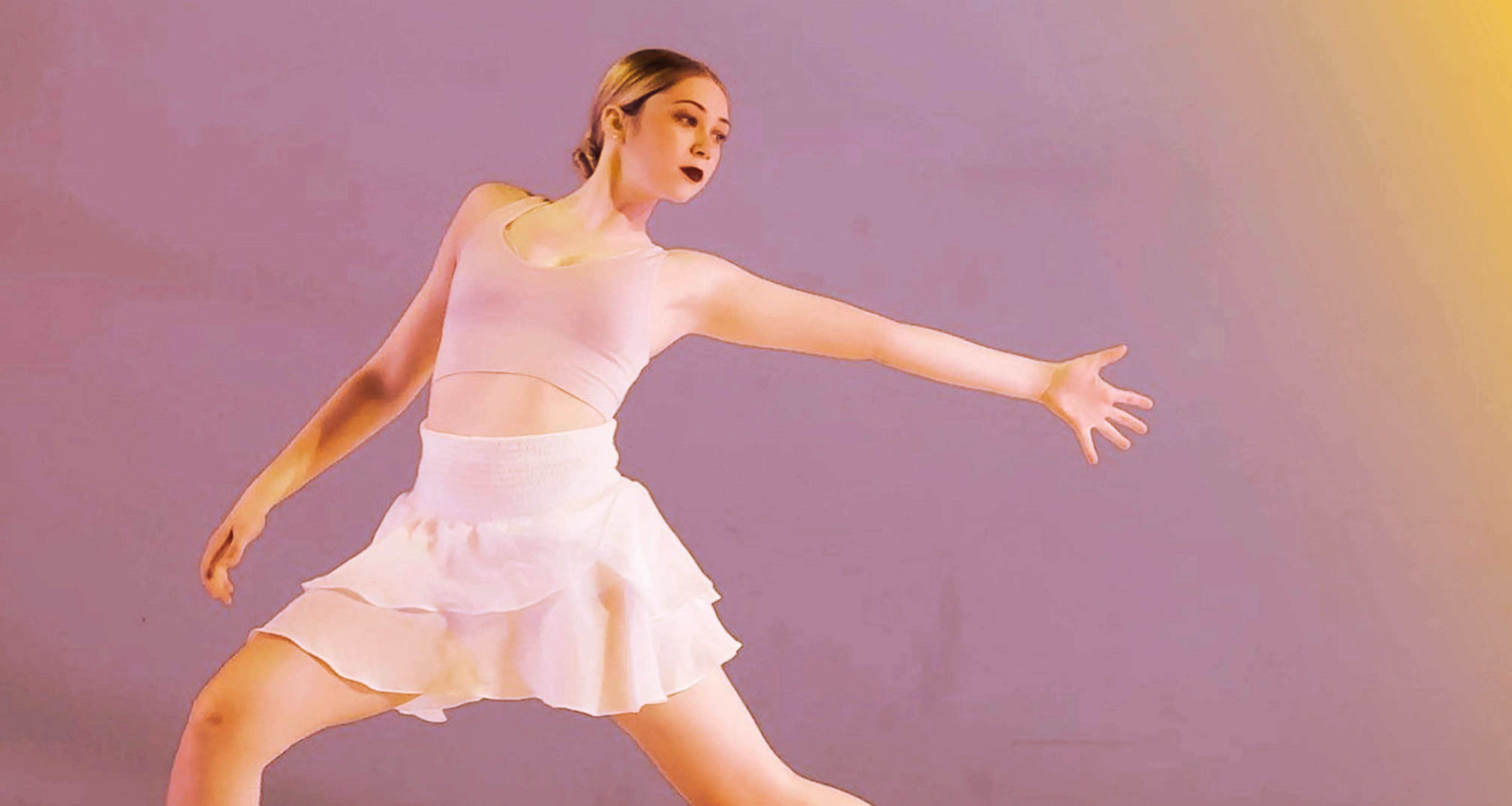 Woman in light pink dance outfit striking a graceful pose with one arm extended against a purple background.