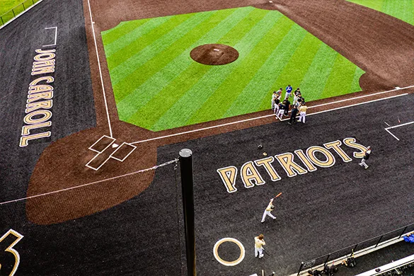 Aerial view of John Carroll's Patriots baseball field with players gathered near home plate.