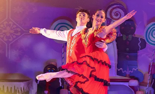 Male and female ballet dancers performing on stage in vibrant red costumes with a candy-themed backdrop.