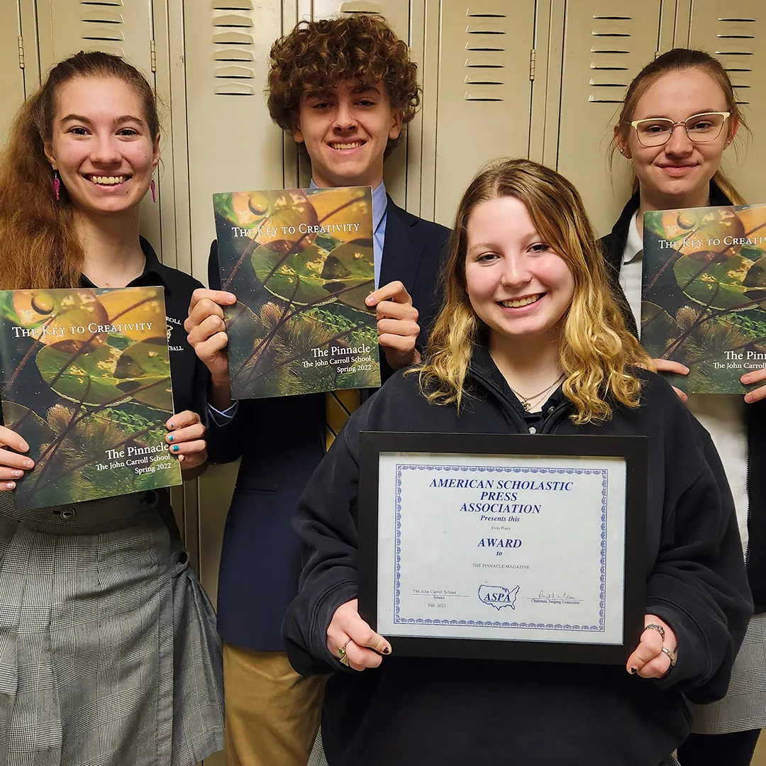 Four smiling students standing in front of lockers holding The Pinnacle magazines and an American Scholastic Press Association award certificate.