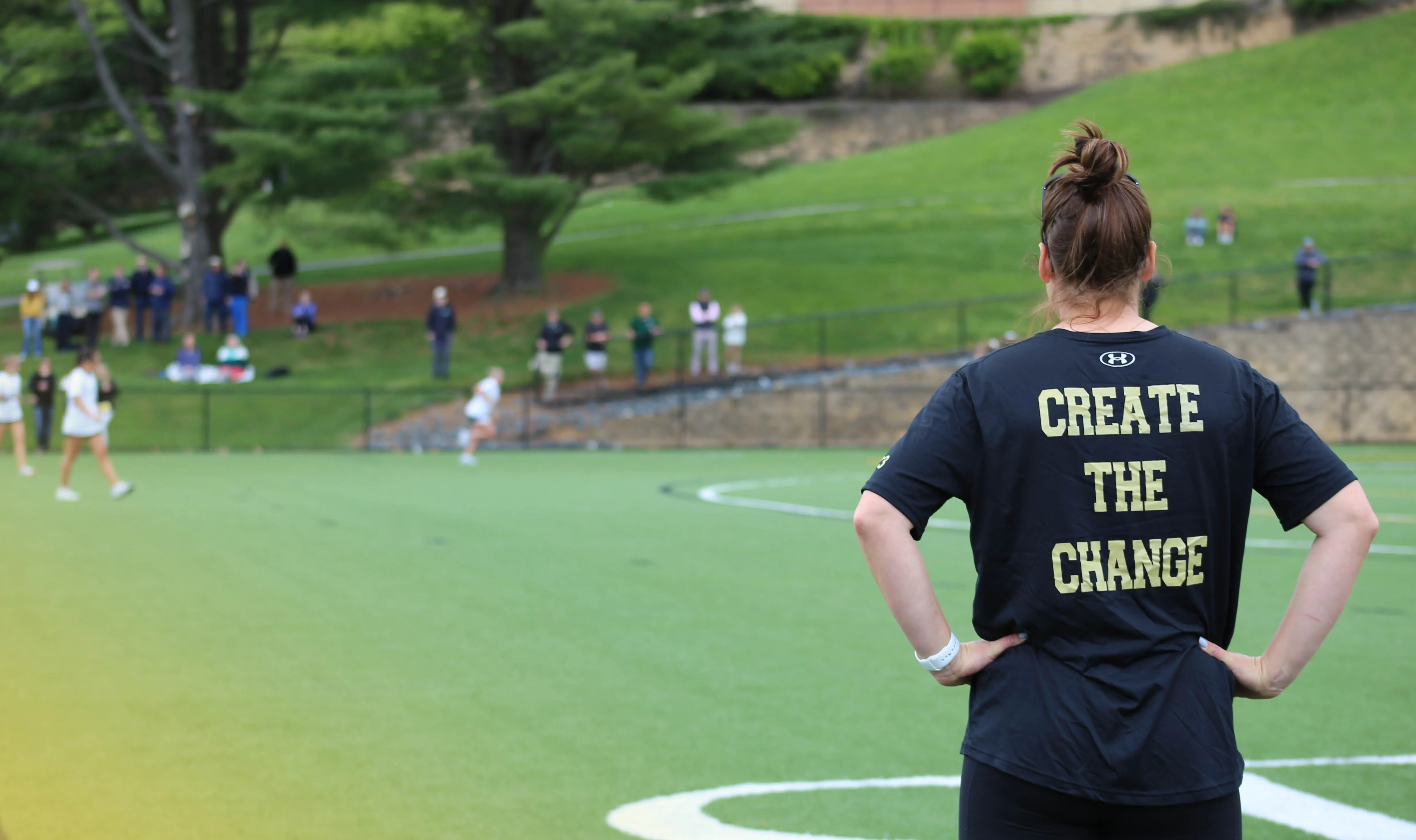 Person standing on a sports field wearing a black shirt with the words 'CREATE THE CHANGE' written on the back.