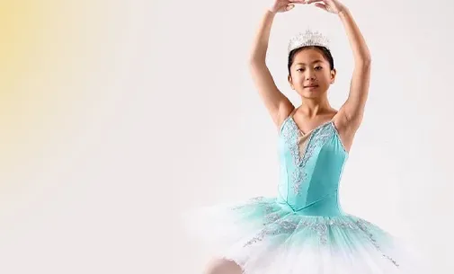 Young ballerina in a light blue tutu and tiara posing with arms raised gracefully.