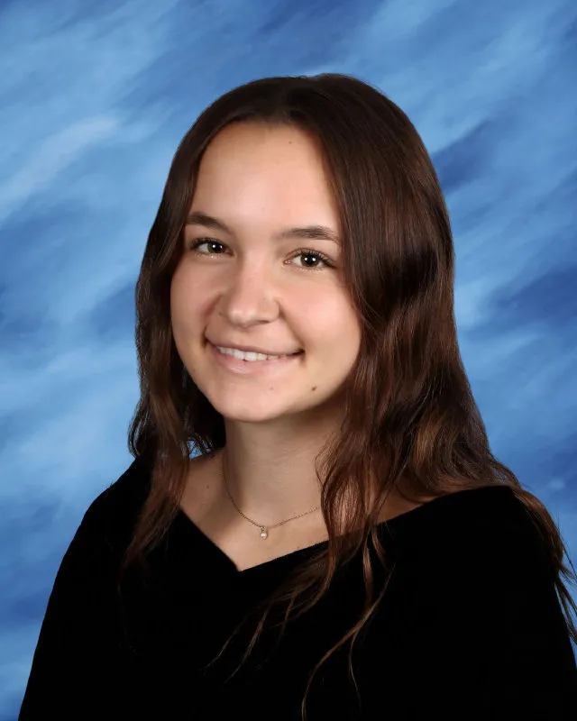 Portrait of a young woman with long brown hair smiling against a blue textured background.