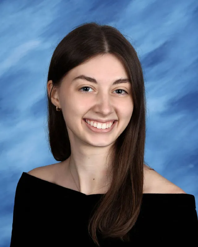 Young woman with long brown hair wearing a black off-shoulder top smiling against a blue textured background.