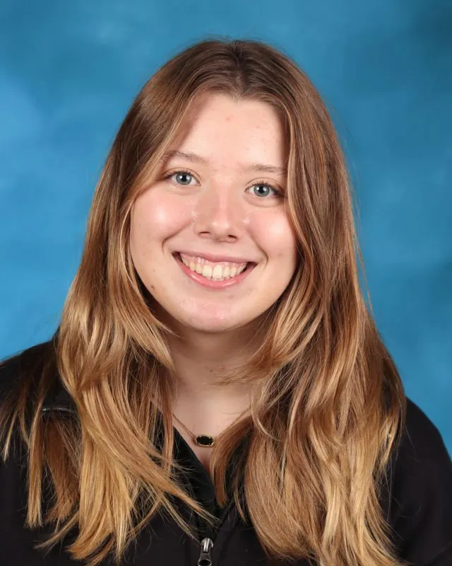 Smiling young woman with long blonde hair against a blue background.