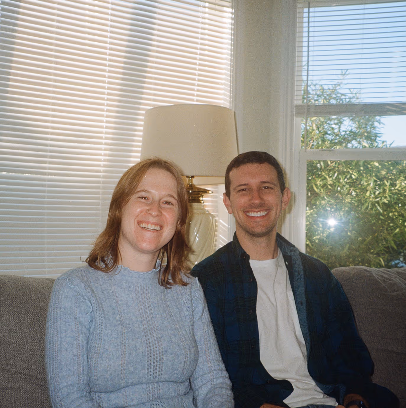 Allswell founders sitting together on a couch in a sunlit room, smiling warmly at the camera.