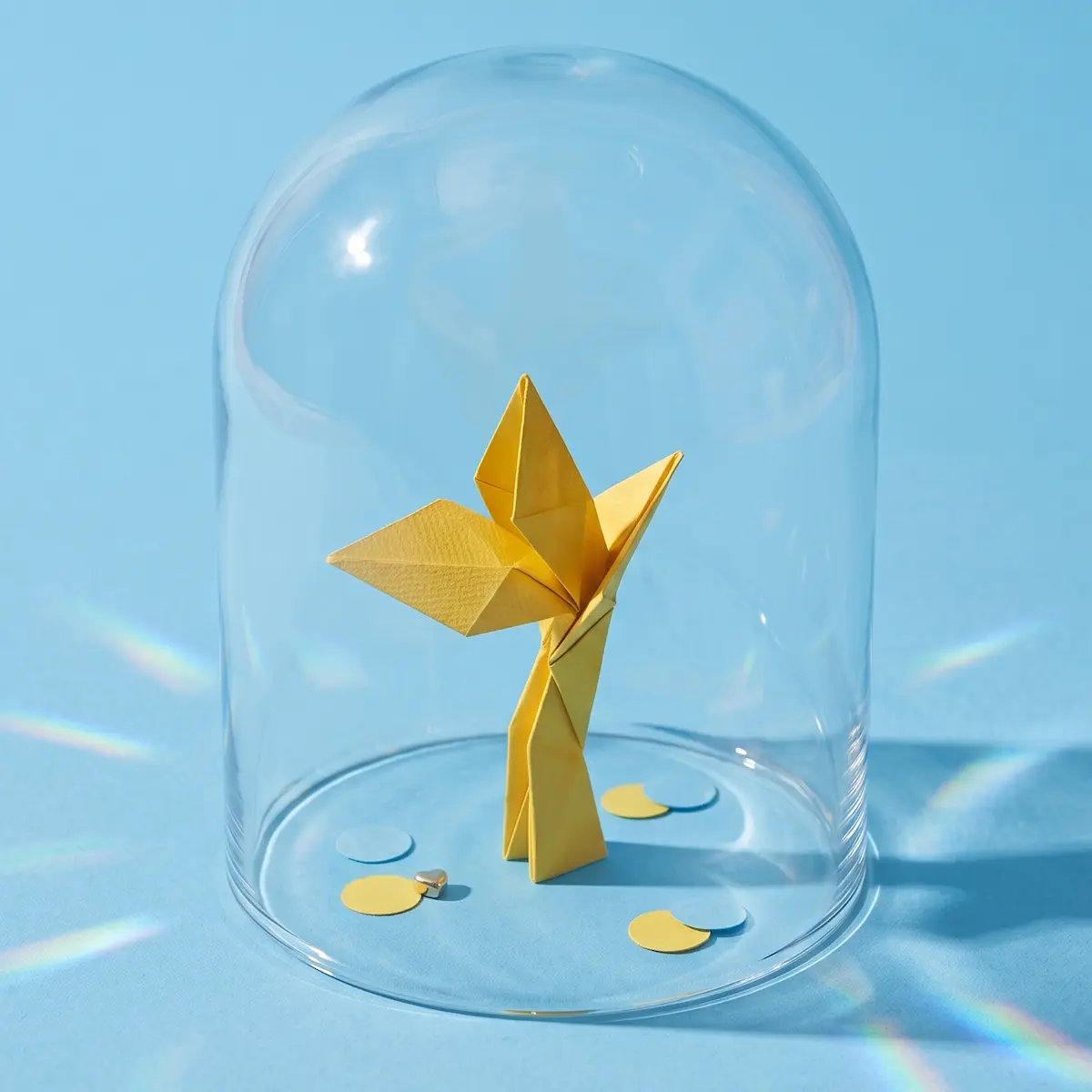 A yellow origami bird standing under a glass display dome