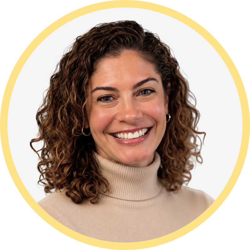 Smiling woman with curly brown hair wearing a beige turtleneck and hoop earrings.