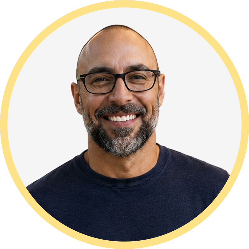 Smiling middle-aged man with glasses, a beard, and a navy blue sweater on a white background.