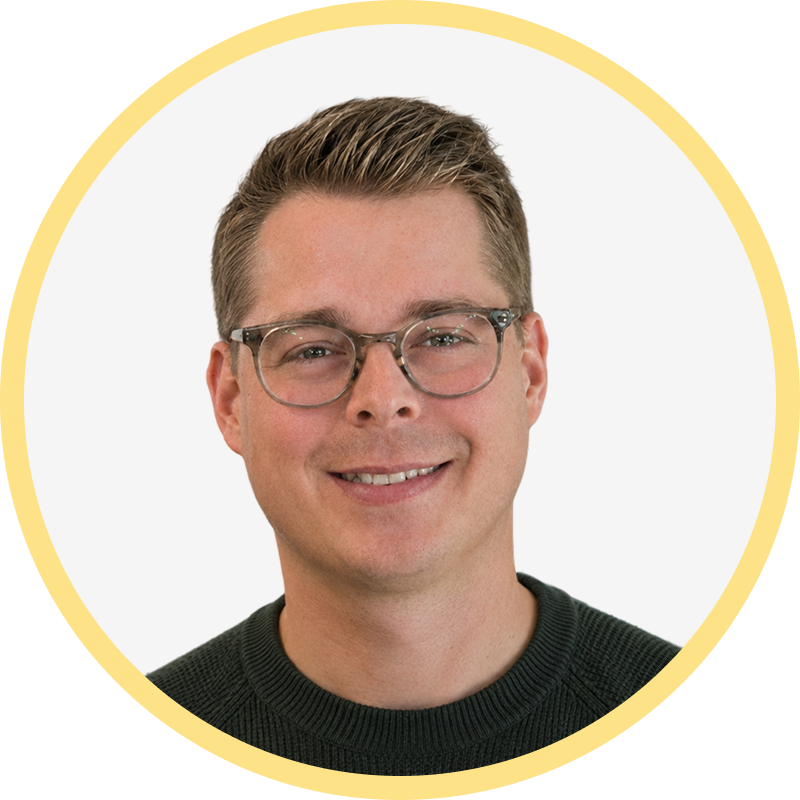 Smiling man with short brown hair, glasses, and a dark green sweater inside a yellow circle frame.