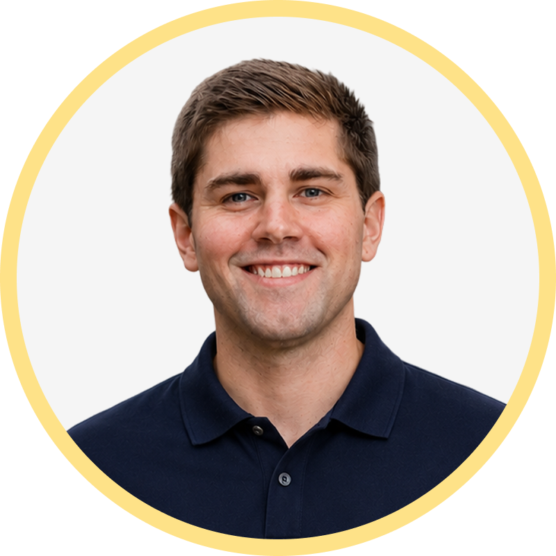Smiling young man with short brown hair wearing a navy blue polo shirt against white background.