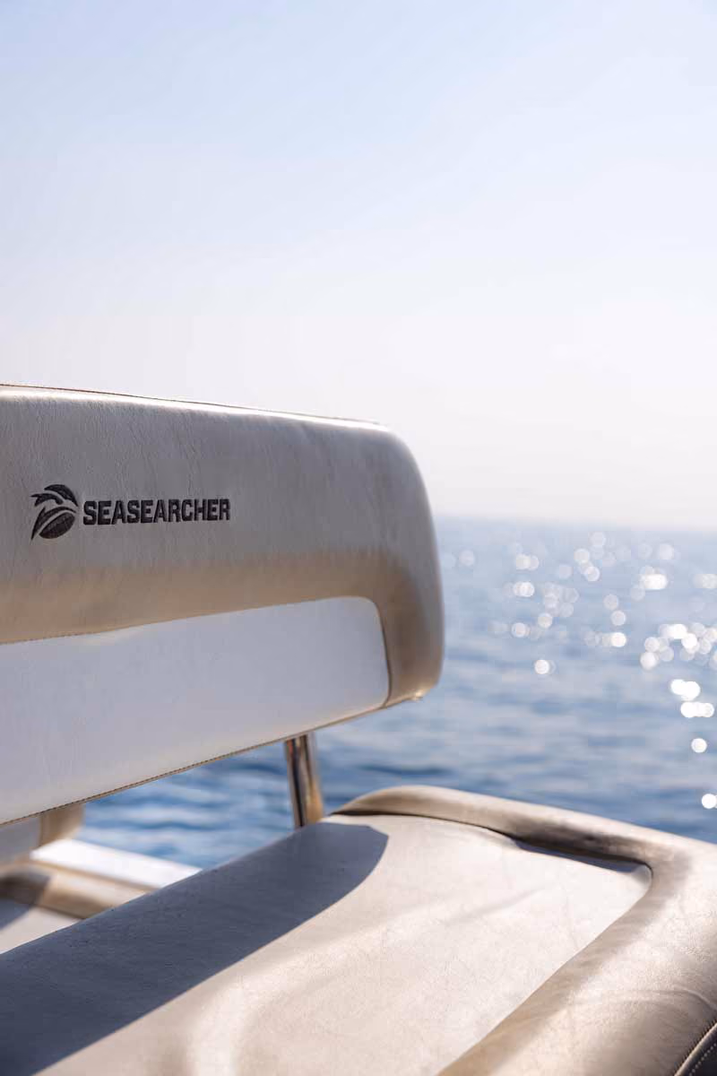 Beige boat seat with SEASEARCHER logo, overlooking a sparkling blue sea under a clear sky.